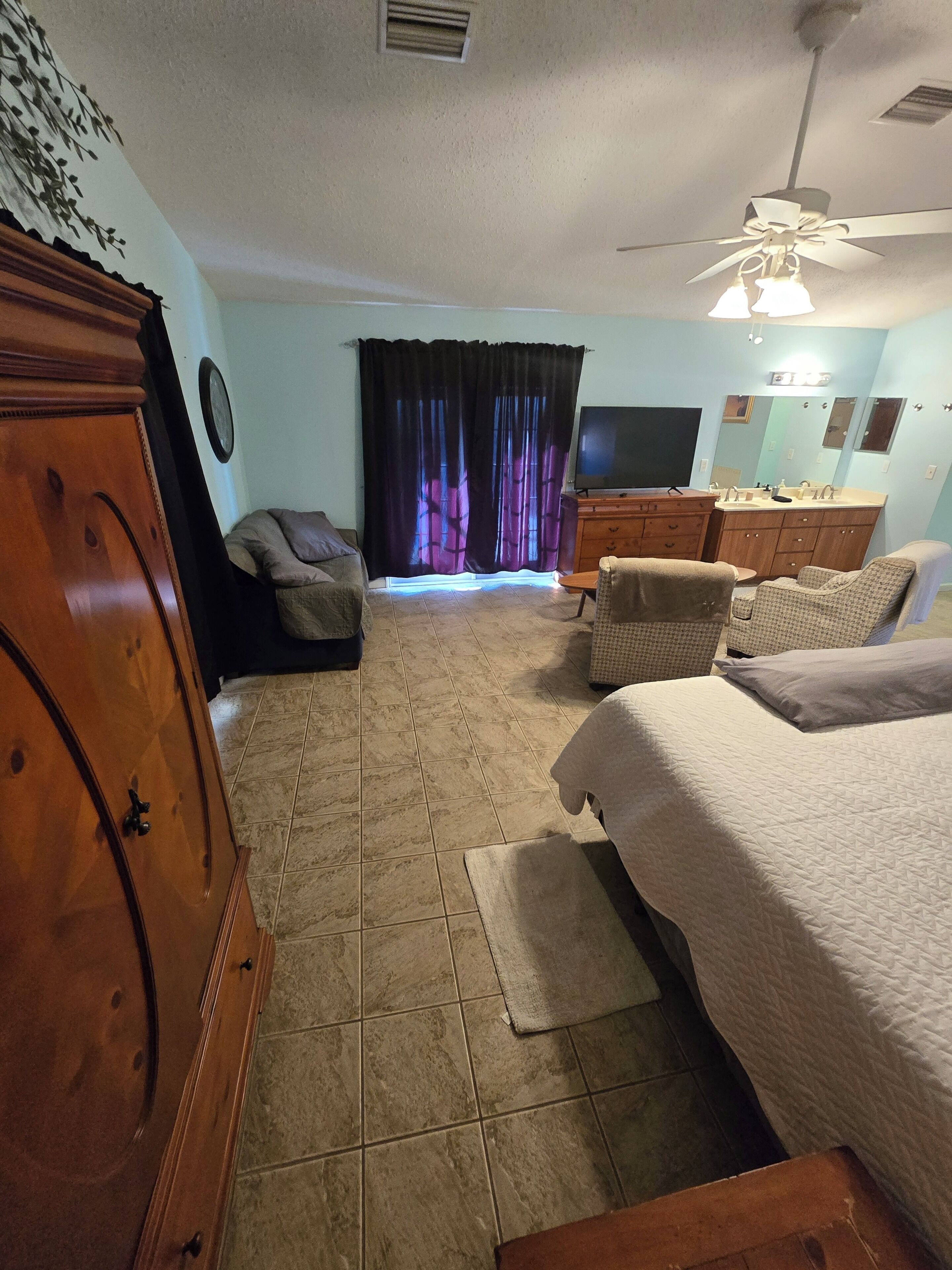 A bedroom with a bed, a dresser, a TV, a ceiling fan, and a window with curtains.