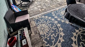 A covered patio with a pool, outdoor furniture, and a patterned rug.