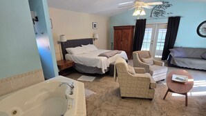 A spacious room with a large bathtub, a bed, a sofa, and a chair.