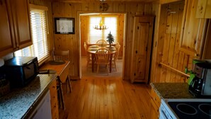 L’intérieur d’un chalet en bois comprend une cuisine, un coin repas et une porte qui donne sur une pièce.