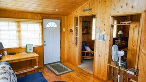 L’intérieur d’une cabine, avec une porte en bois, un bureau, une chaise, un lit et une petite table sur laquelle se trouve une lampe.
