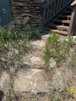 Un sendero de piedra que lleva a una terraza de madera con un muro de piedra y una escalera.
