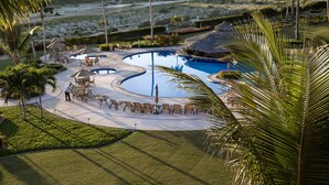Zona de piscina en un resort con sillones de descanso, una cabaña de techo de paja y un césped bien cuidado.