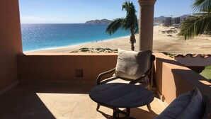 Un balcón con vistas a una playa, una silla y una mesa.