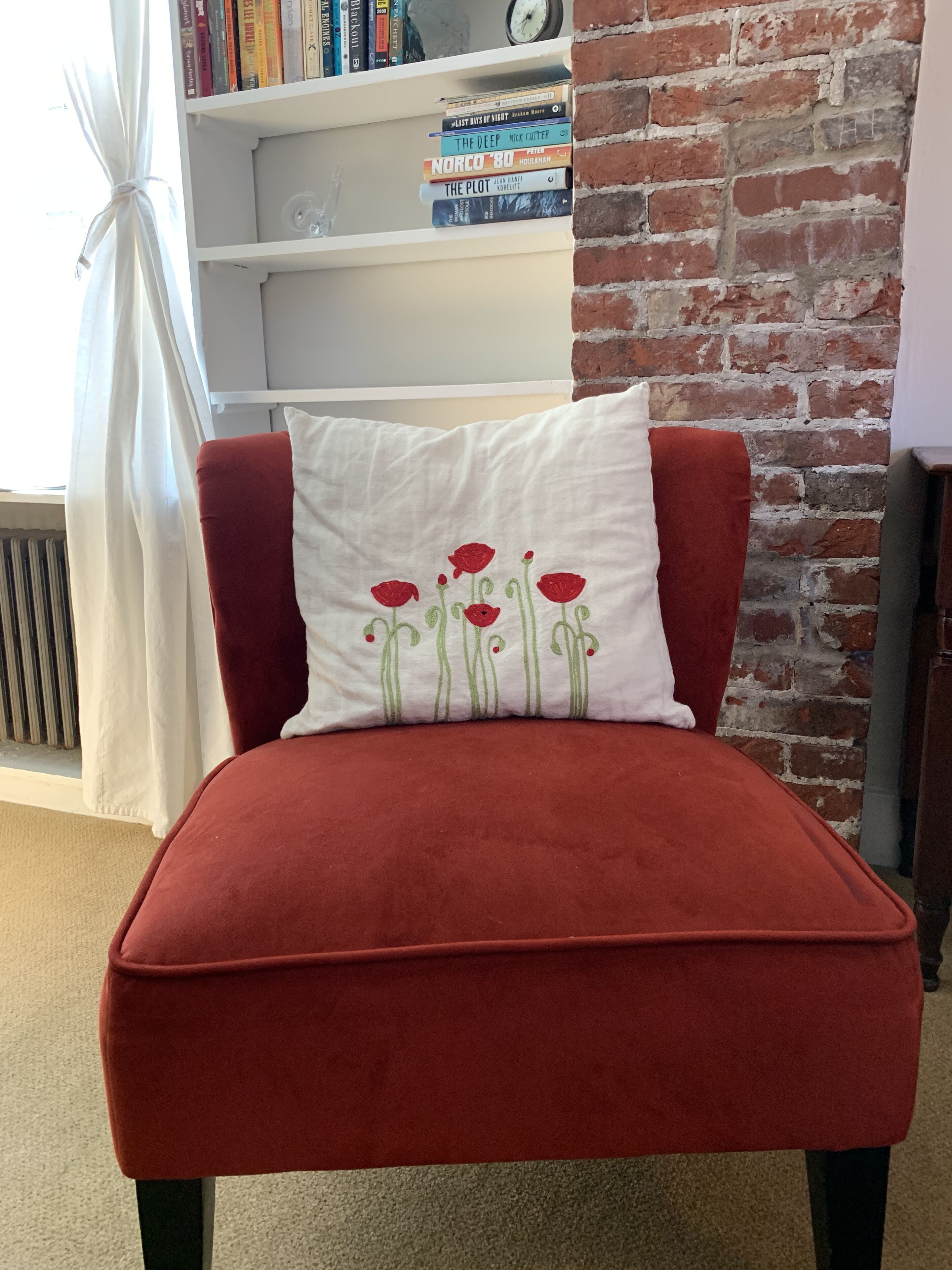 A red upholstered chair with a white pillow featuring red flowers.
