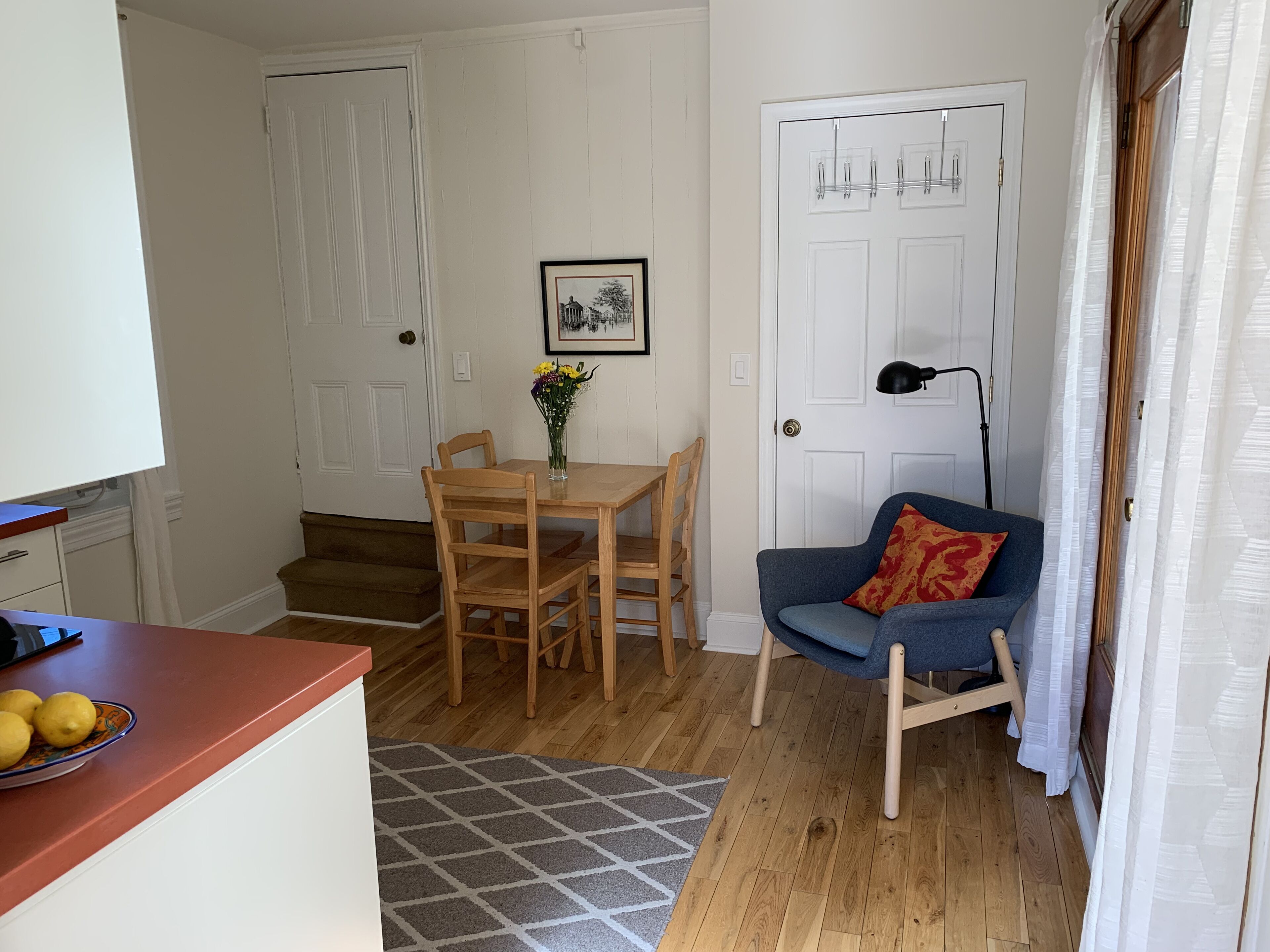 Un espace de vie compact comprenant un coin repas, un canapé, un escalier et une porte avec un porte-manteau.