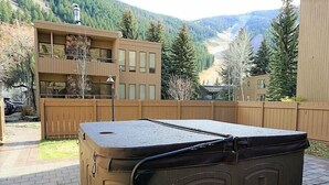 A hot tub in a backyard with a wooden fence, a stone wall, and a mountain view. - Sawtooth Condo at Warm Springs Base (Ketchum)
