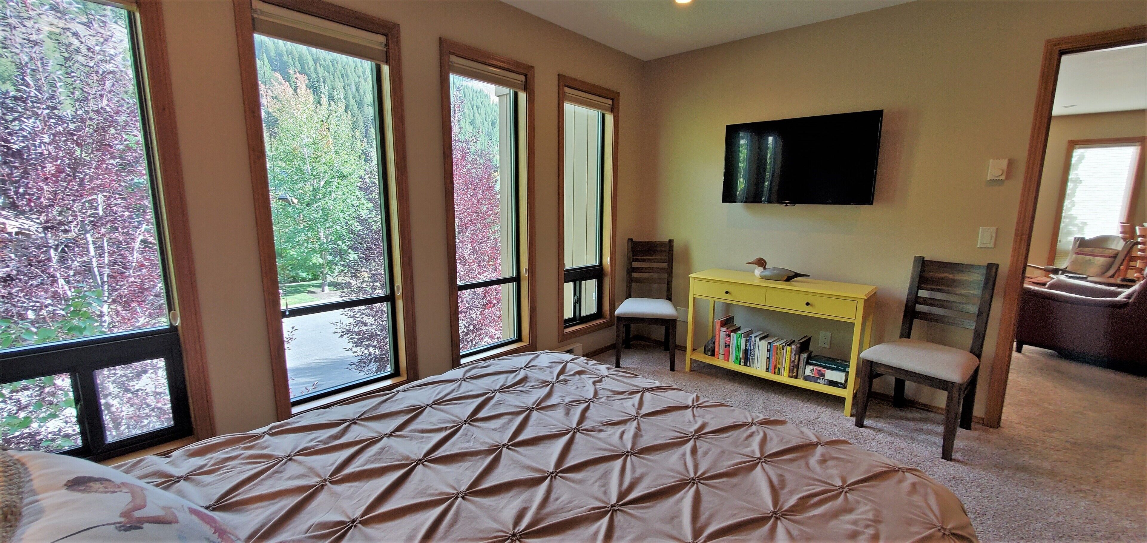 A bedroom with a large bed, a TV mounted on the wall, and a bookshelf.