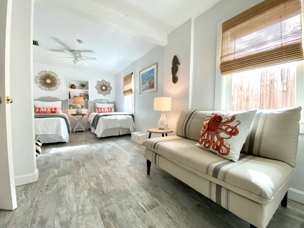 A well-lit bedroom with a bed, a nightstand, a bedside table, a ceiling fan, and a window with blinds.