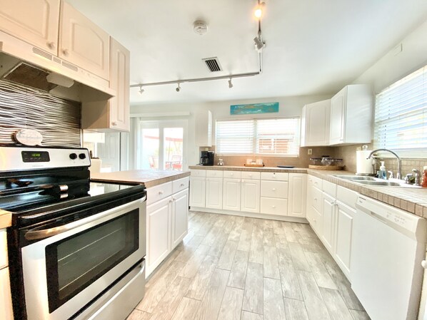 A modern kitchen with white cabinetry, a stove, and a large window providing natural light. - Paradise Found in the heart of Flagler Beach (Flagler Beach)