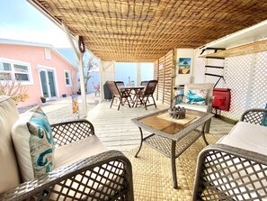 A covered outdoor seating area with wicker furniture, a table, and a view of a building in the background.