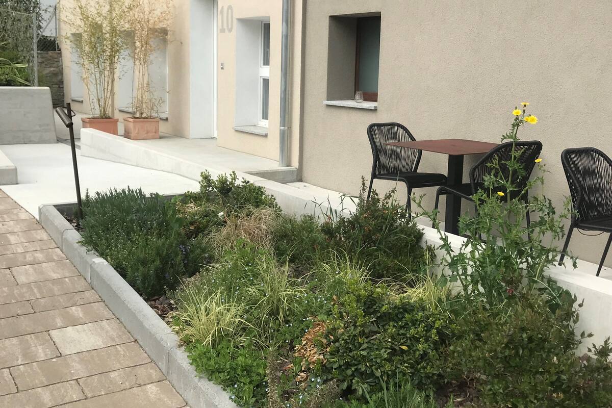 Un patio con mesa y sillas, una ventana pequeña y una planta en maceta.