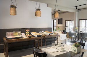 Uma área de refeições com mesa de madeira posta para o café da manhã, um buffet com diversos alimentos e luminárias pendentes de madeira.