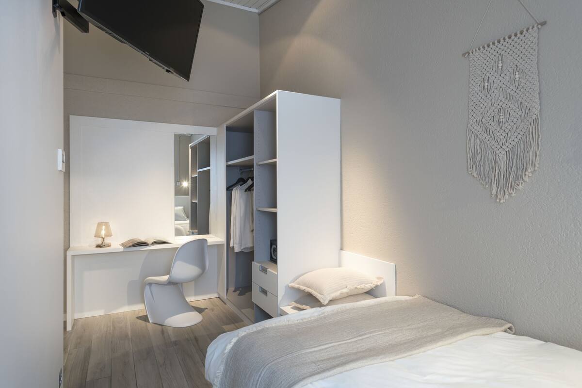 Un dormitorio moderno con cama, escritorio, silla y armario.