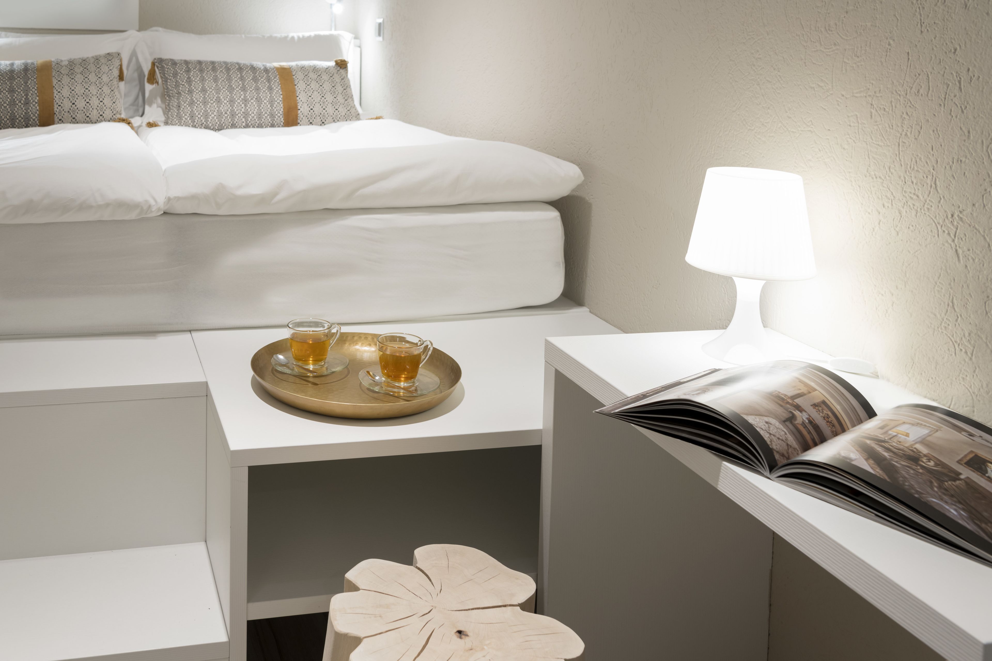Une chambre d’hôtel bien rangée, avec un lit, une table de chevet dotée d’une lampe, un plateau avec des boissons et un magazine.