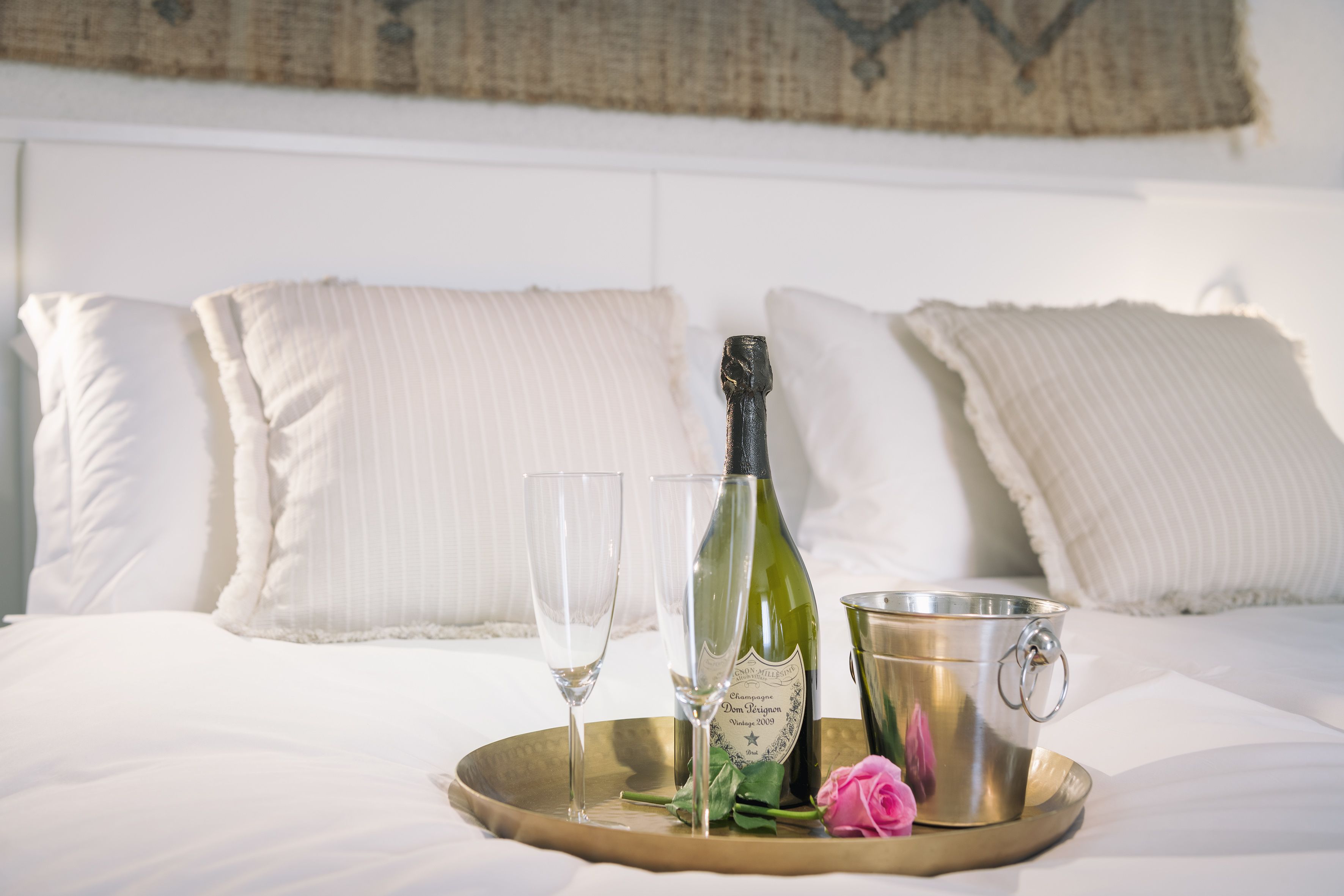 Een bed met witte beddengoed, twee lege glazen, een fles champagne en een metalen emmer op een dienblad.