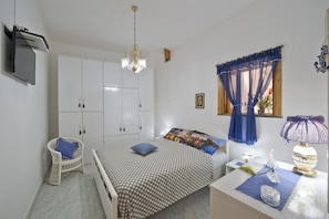 A bedroom with a bed, a chair, a desk, a chandelier, and a window with curtains.