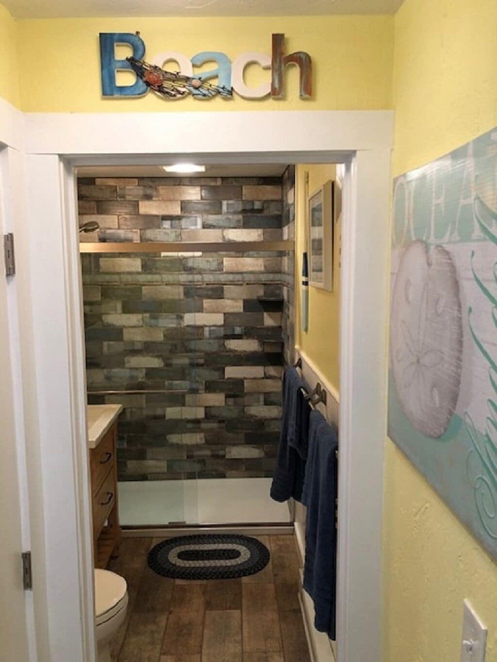 A bathroom with a stone mosaic wall, a toilet, a sink, and a towel rack.