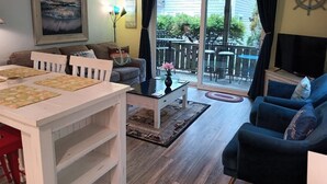 Sala de estar com uma mesa branca, sofá azul e uma grande janela com vista para o exterior.