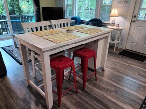 A dining area with a white table, red stools, and a window with a view of trees. - RECENTLY RENOVATED 2 BEDROOM CONDO WITH DECK & OFF STREET PARKING CLOSE TO BEACH (Provincetown)