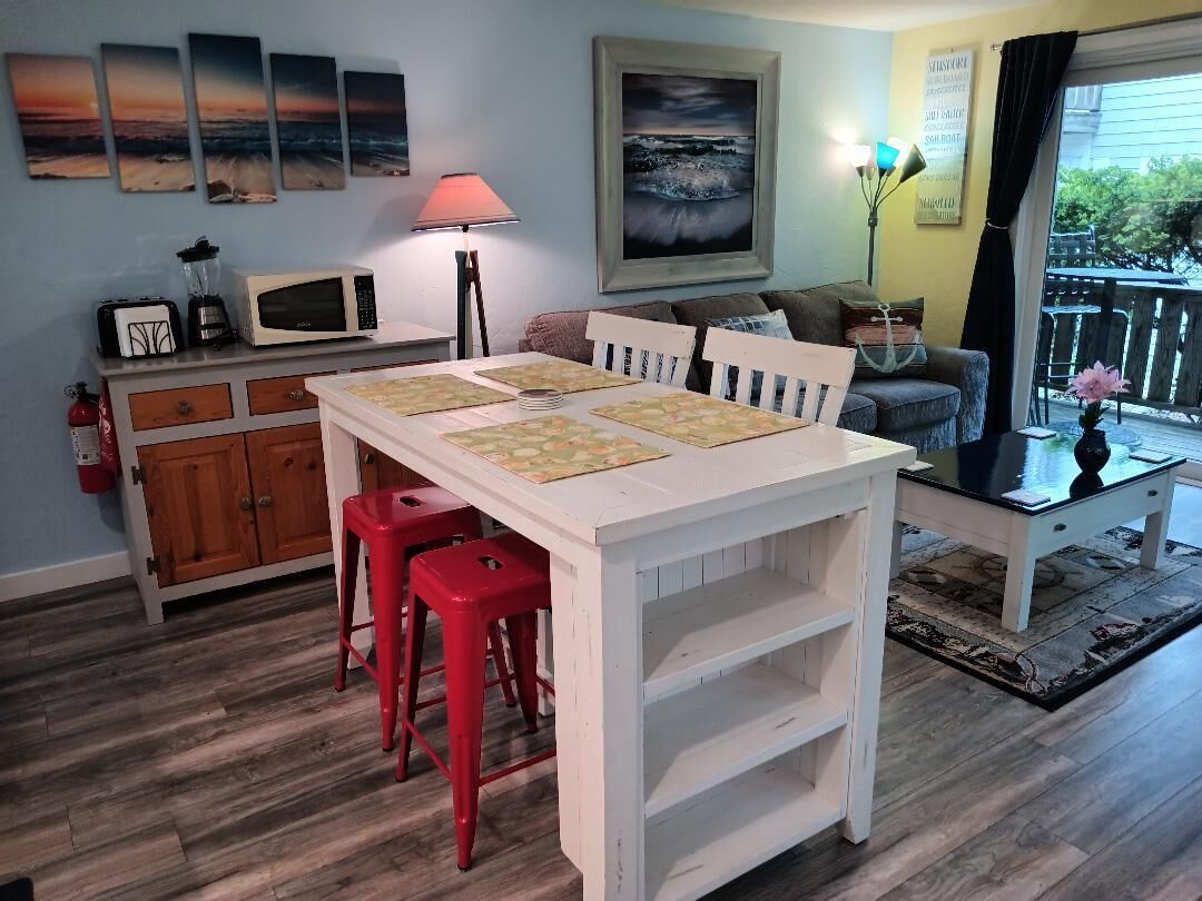 A dining area with a white table, red stools, a microwave, and a painting on the wall.