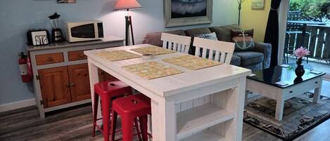 A dining area with a white table, red stools, a microwave, and a painting on the wall.