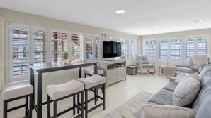 A modern living room with a kitchen area, a TV, and a bar with stools.