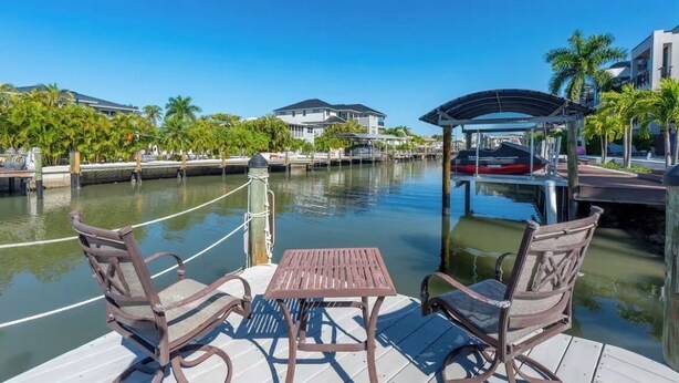 A waterfront deck with a table and chairs, a covered seating area, and a view of the water and buildings.