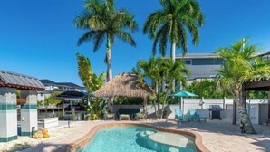A swimming pool surrounded by palm trees and a thatched-roof structure.
