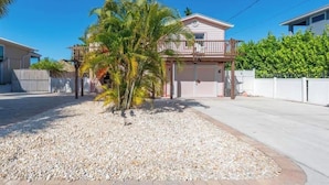 A two-story house with a balcony, a garage, and a small palm tree in the front yard.