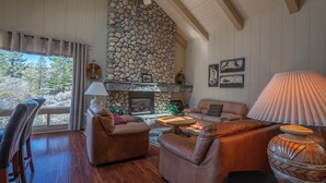 Un salon chaleureux avec des canapés en cuir, une cheminée en pierre et une grande fenêtre donnant sur une forêt.