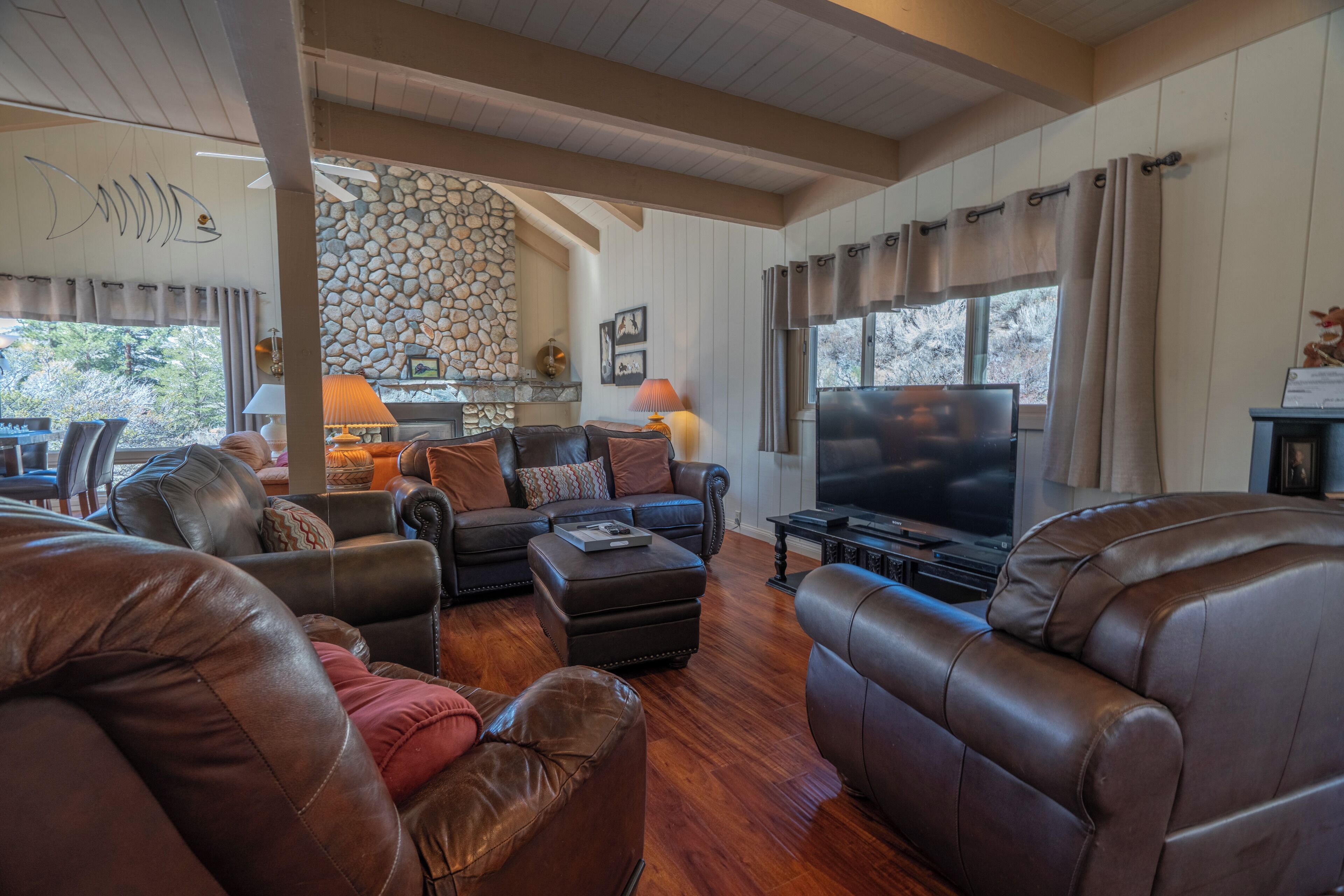 A spacious living room with leather sofas, a flat-screen TV, and a stone fireplace.