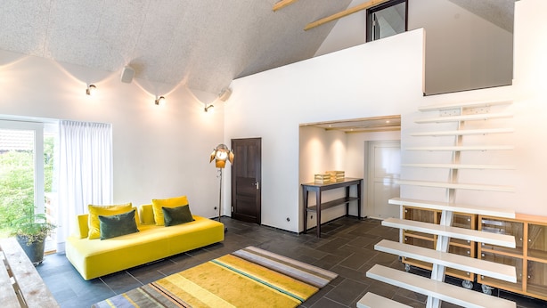 A modern living room with a yellow sofa, a wooden bench, and a dining area with a table and chairs. - Trädgårdshuset i Sankt Olof (Sankt Olof)