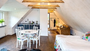 A cozy attic bedroom with a bed, a dining table with chairs, and a kitchenette. - Trädgårdshuset i Sankt Olof (Sankt Olof)
