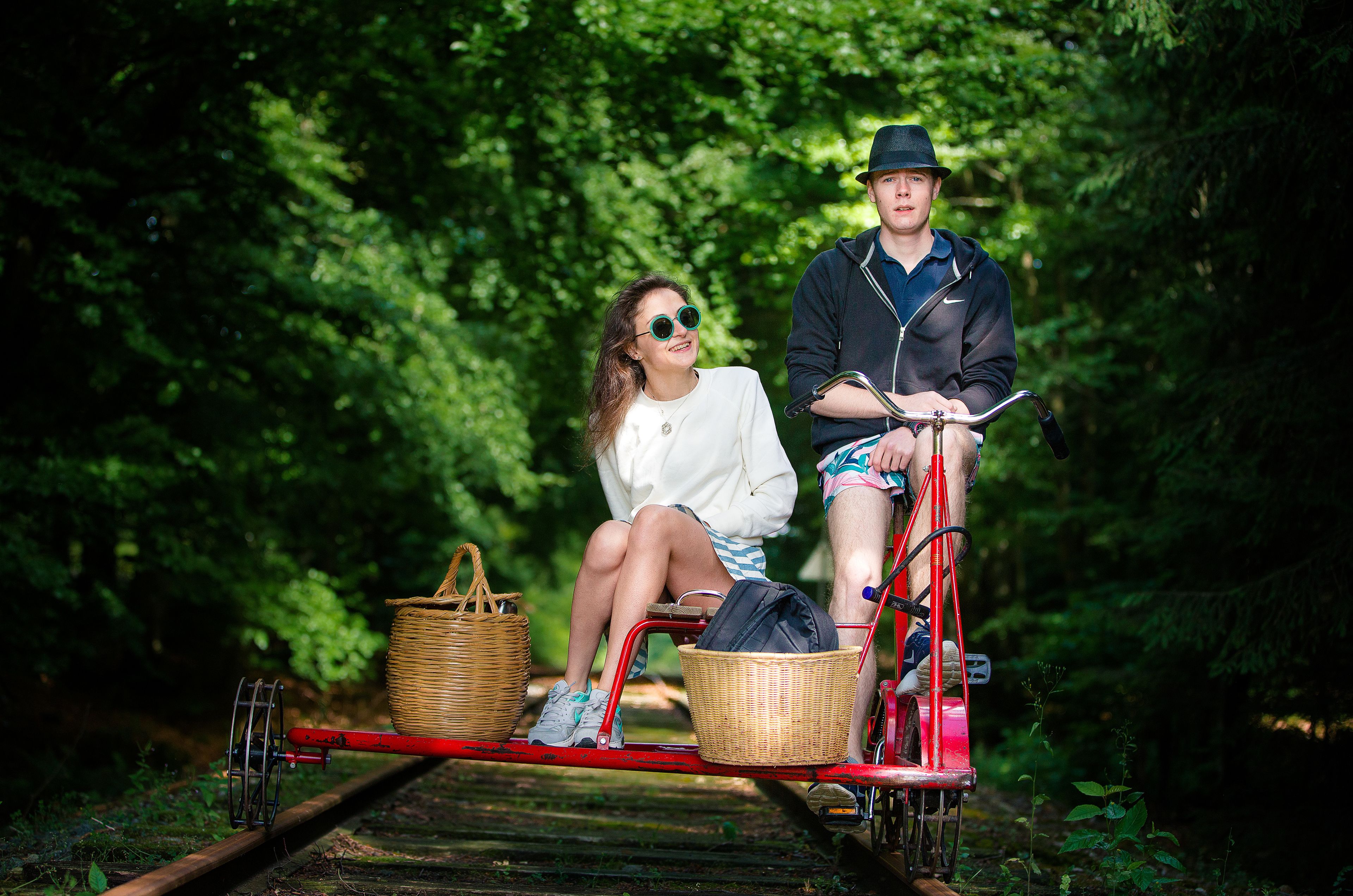 Two people sitting on a bicycle on a railway track surrounded by greenery.