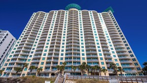 Un hotel moderno di grandi dimensioni con numerosi balconi, un design architettonico curvo e palme sullo sfondo.