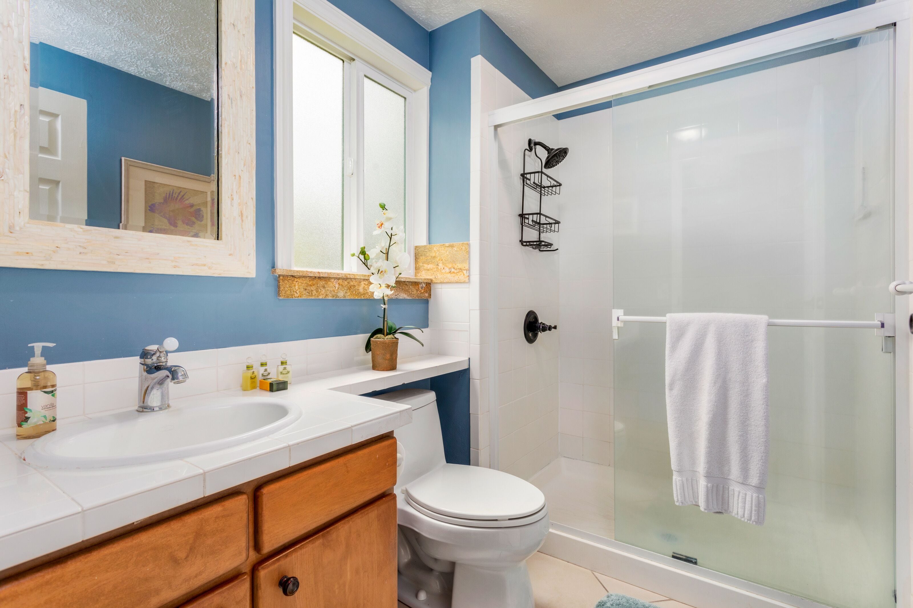 Un baño con lavamanos blanco, un espejo, inodoro y cabina de ducha de cristal.