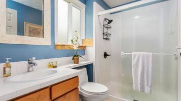 Un baño con lavamanos blanco, un espejo, inodoro y cabina de ducha de cristal.
