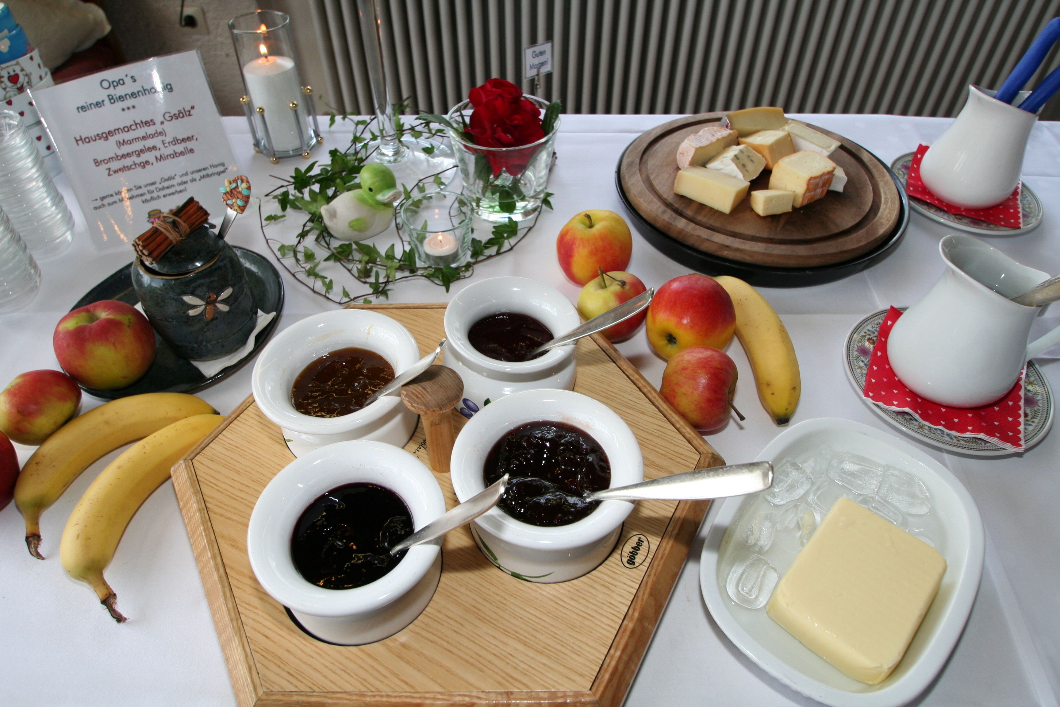 Una mesa con diversos alimentos, como manzanas, plátanos, queso y frascos de mermelada.