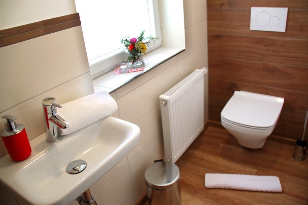 Un baño con lavamanos blanco, dispensador de jabón rojo y un inodoro.