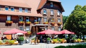 A traditional European-style building with a brick facade, multiple windows, and outdoor seating with red umbrellas.