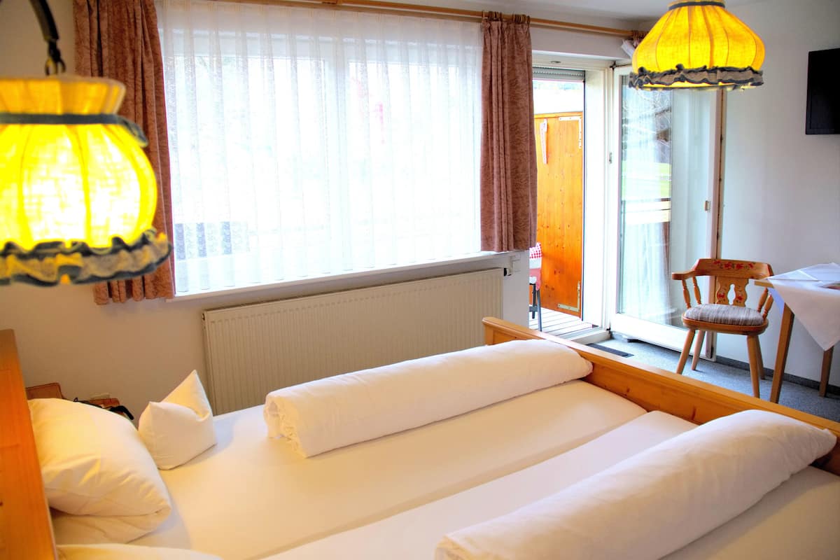Une chambre d’hôtel avec deux lits, une fenêtre avec des rideaux, une table avec une chaise et une lampe.