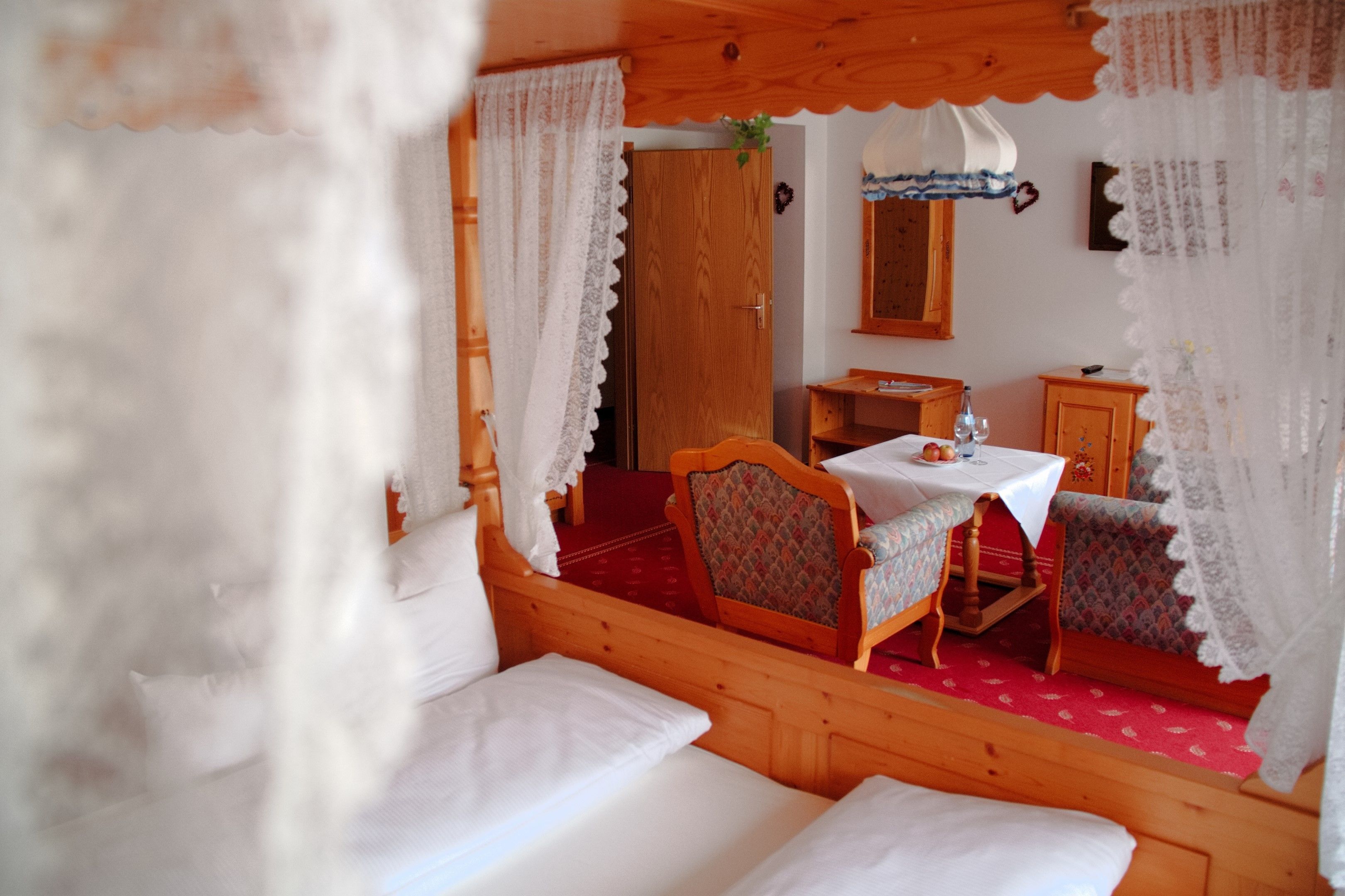 A cozy room with a wooden bed, a small table with a white tablecloth, and a chair.