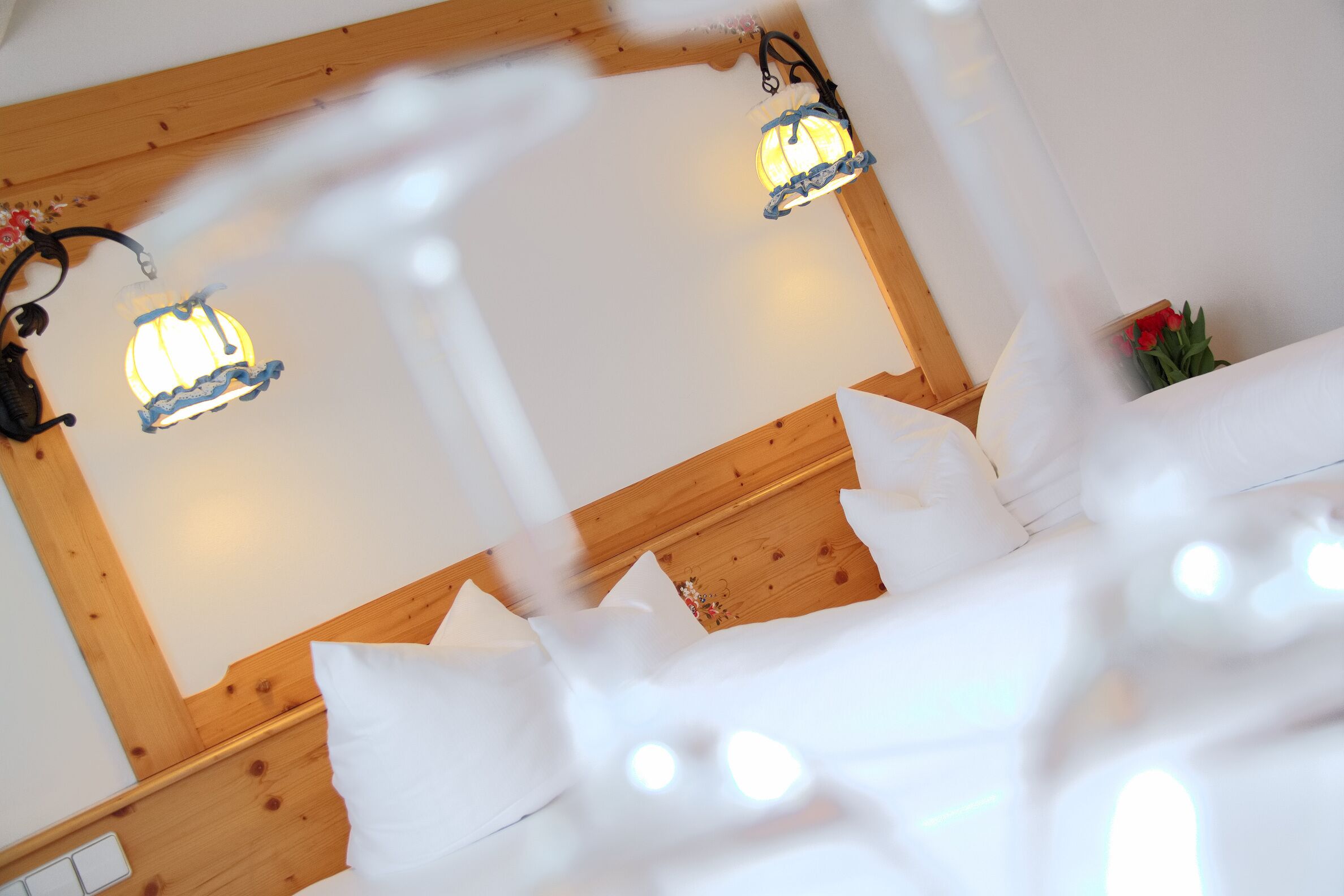 A hotel room with wooden headboard, white bedding, and two wall-mounted light fixtures.
