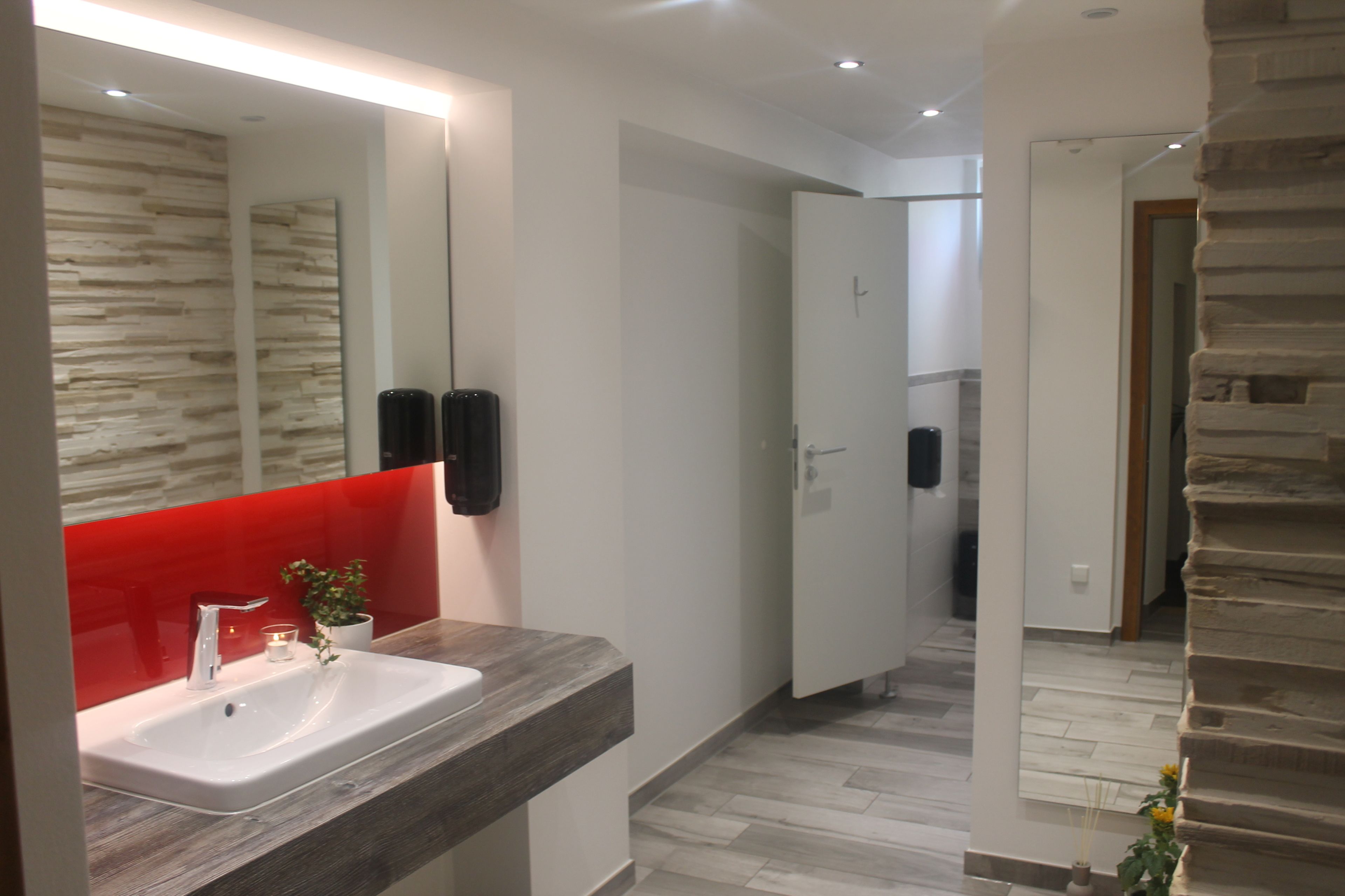A modern bathroom with a white sink, a red accent wall, and a large mirror.