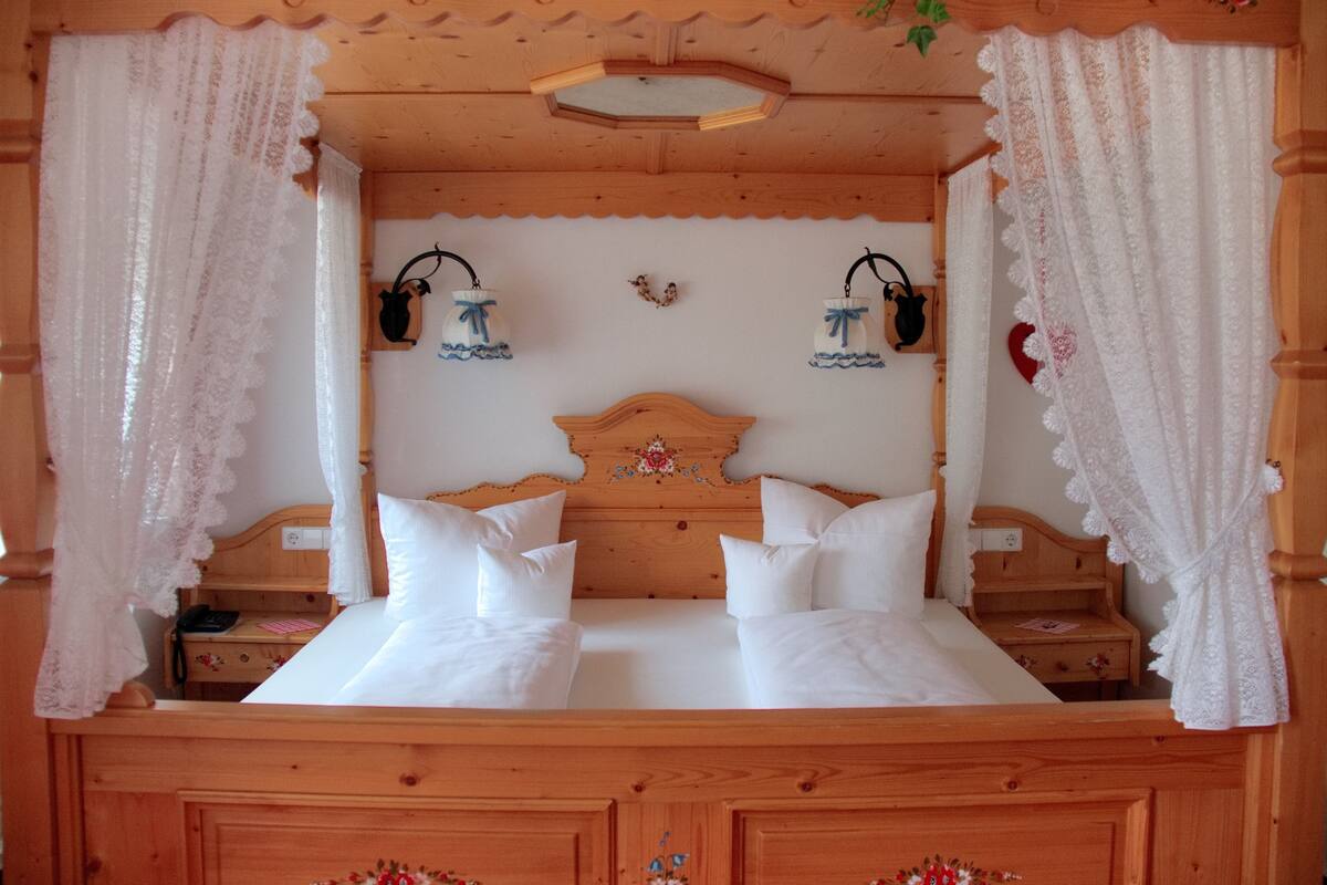 Un lit à baldaquin en bois, avec du linge de lit blanc, deux tables de chevet et une tête de lit à motifs floraux.