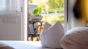 A hotel room with a bed, pillows, a window, and a view of a balcony with plants.