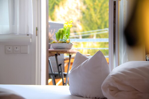 A hotel room with a bed, pillows, a window, and a view of a balcony with plants. - Gasthaus Adler Fohrenbühl (Lauterbach)
