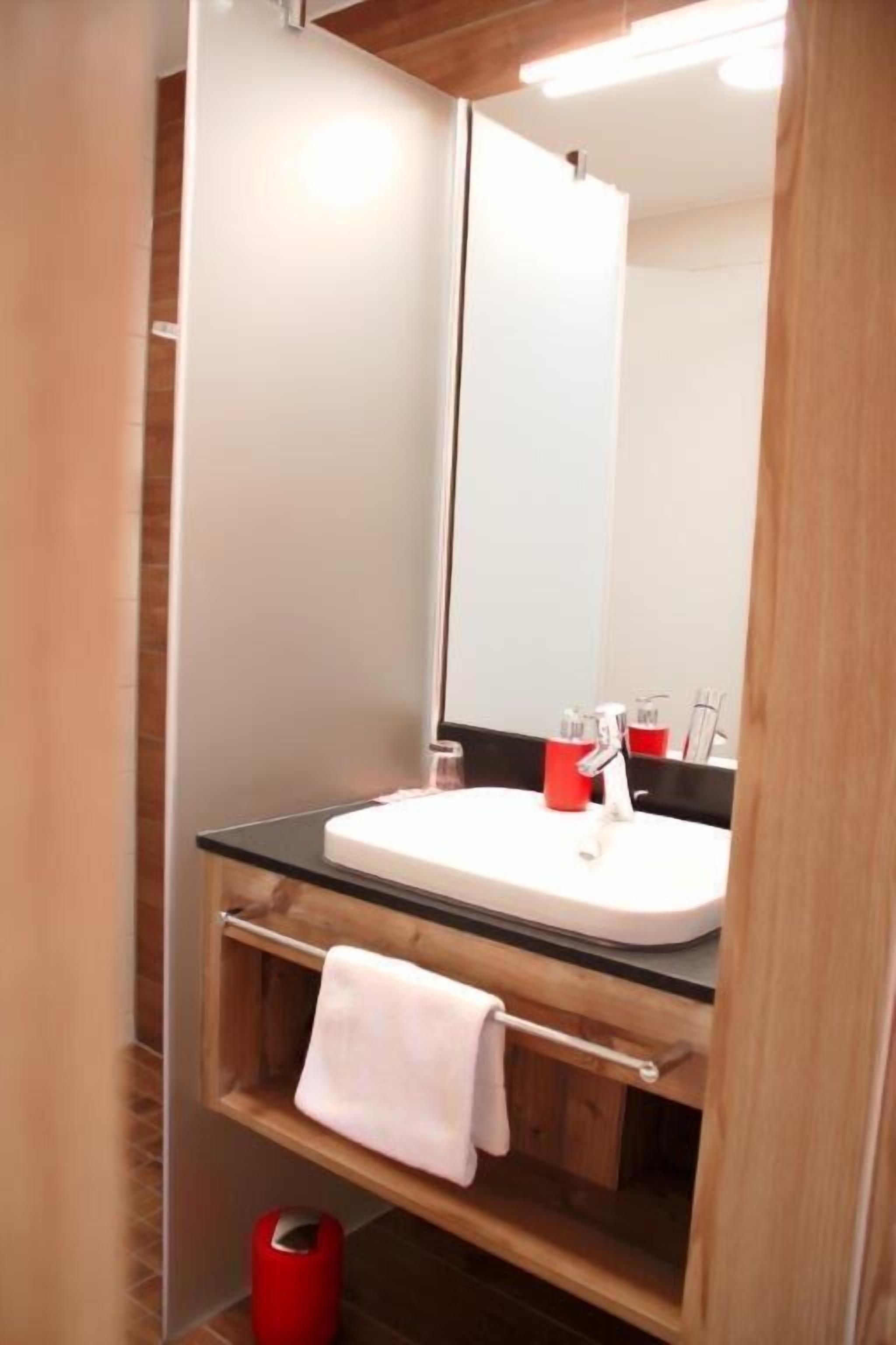 A modern bathroom with a glass sink, wooden vanity, and a large mirror.