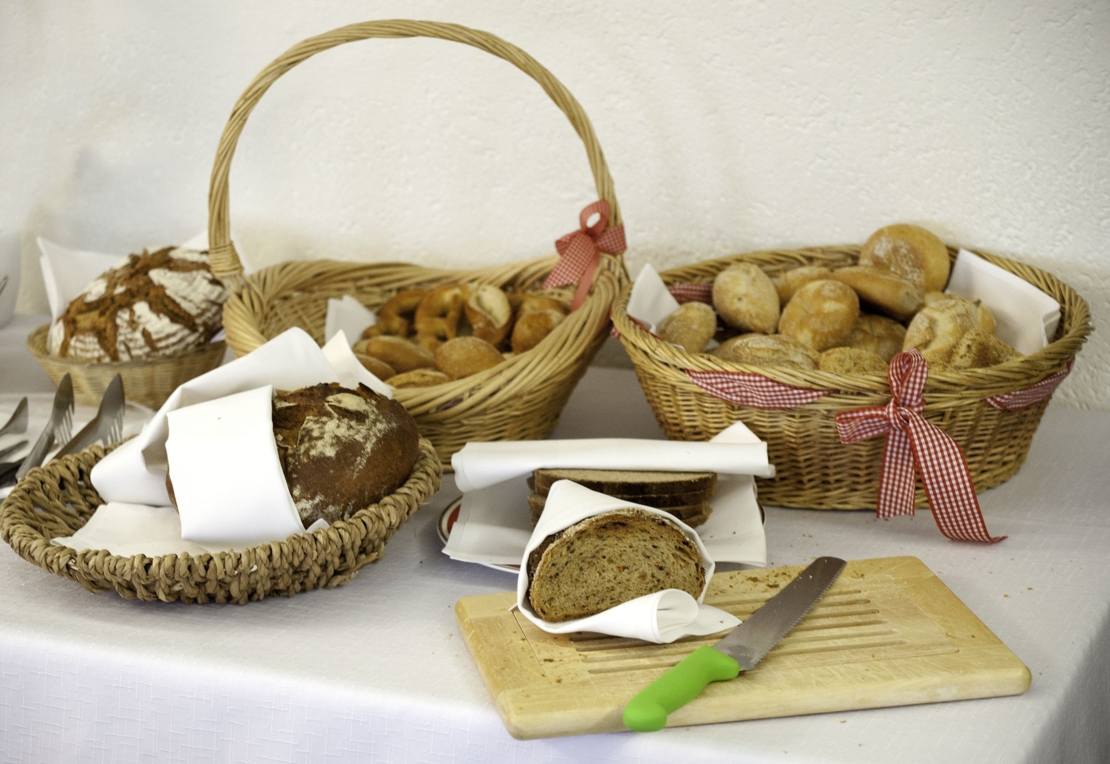 Tre cesti di vimini pieni di pane, un tagliere con un coltello e una tovaglia bianca.
